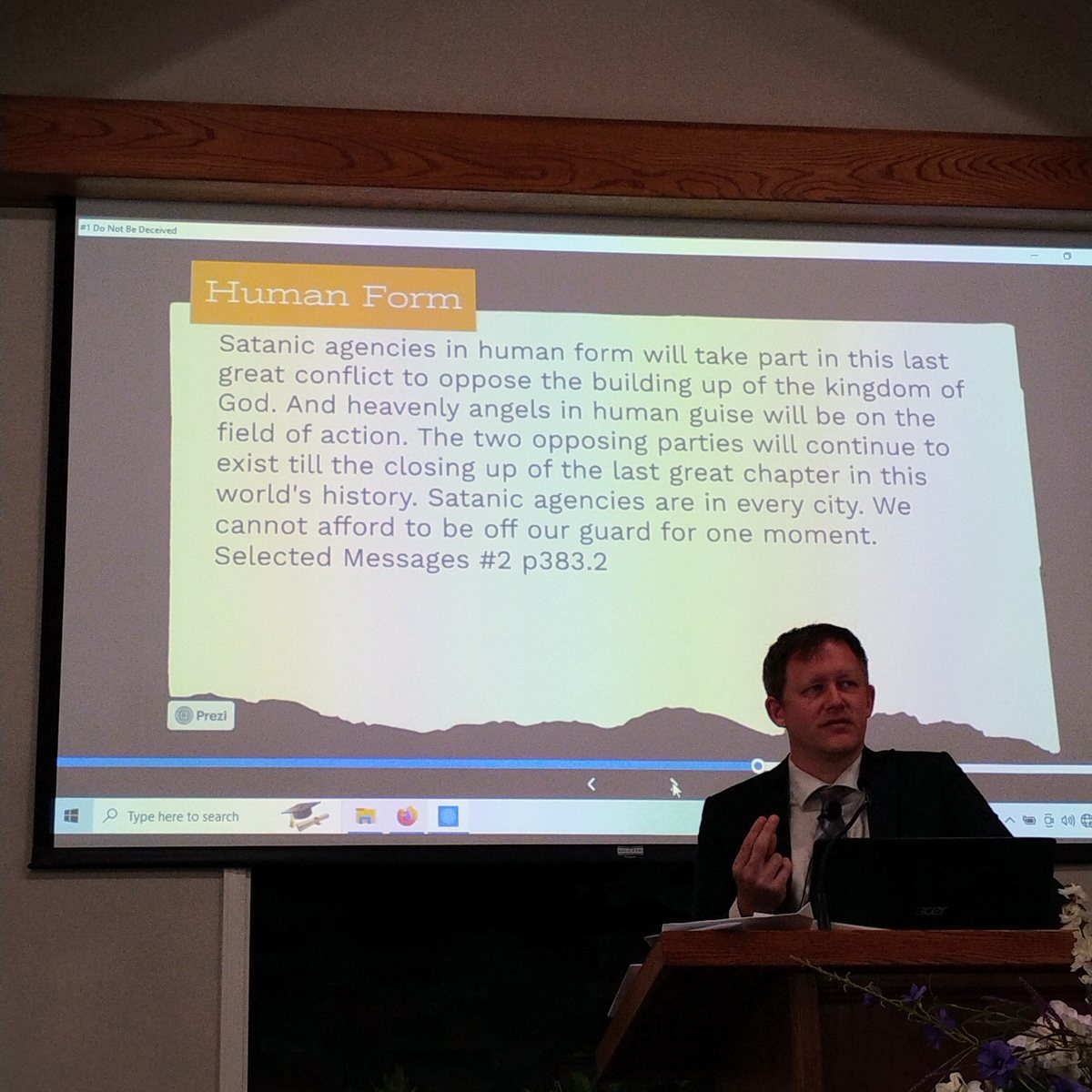 A presentation lit by a projection screen displaying a slide on satanic agencies in human form