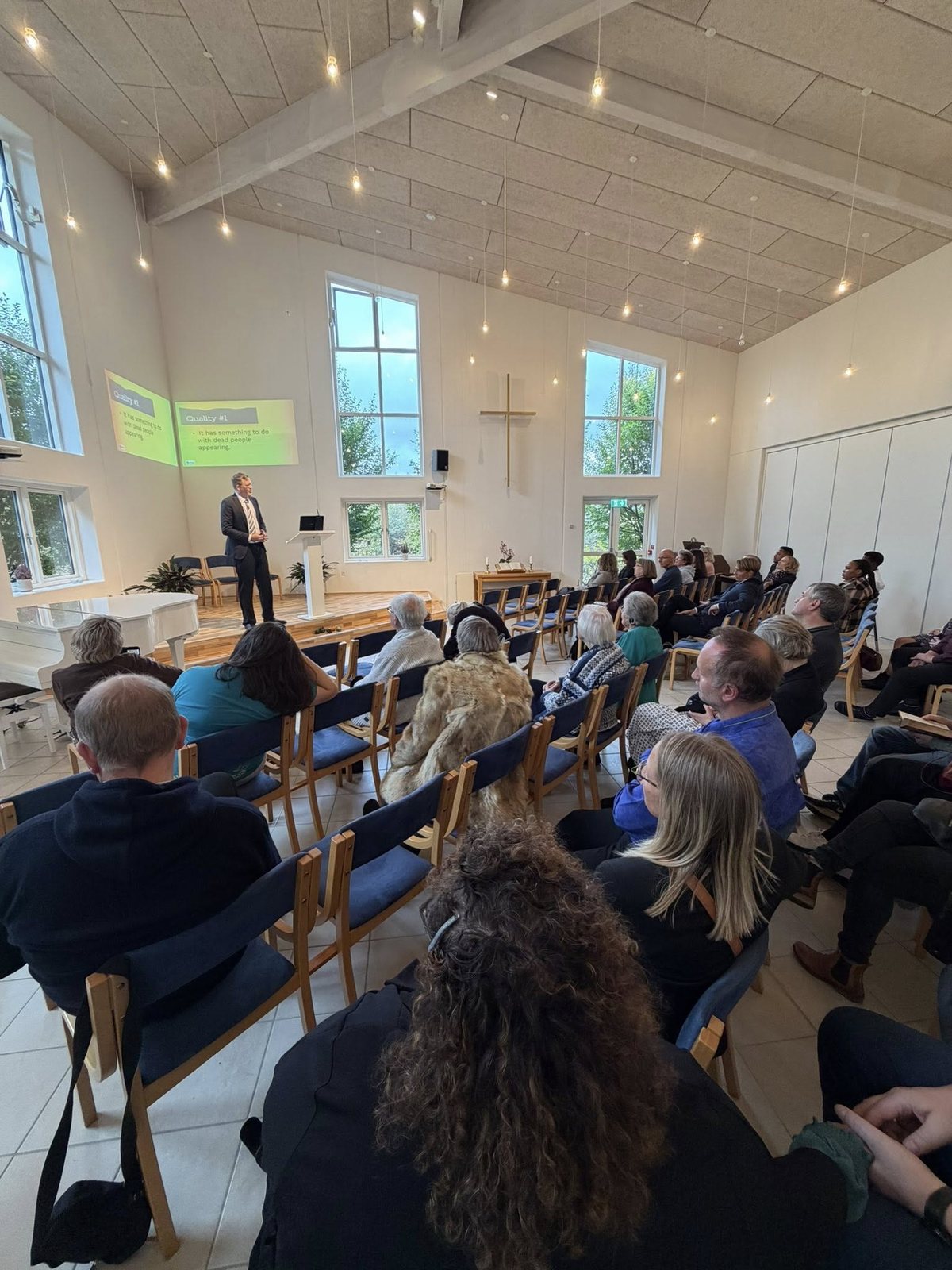 A congregation seated in a bright sanctuary watching a Strange Normal presentation
